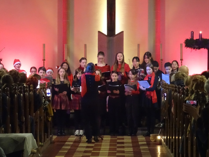 KI generiert: Eine Gruppe von Menschen, wahrscheinlich ein Chor, singt in einem dekorierten Innenraum, möglicherweise während einer Weihnachtsveranstaltung. Die Szene wird von Kerzenschein und stimmungsvoller Beleuchtung untermalt.