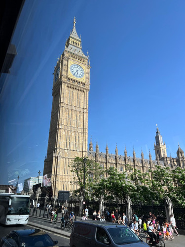 KI generiert: Das Bild zeigt den Big Ben in London unter einem klaren blauen Himmel. Im Vordergrund sind viele Menschen und Fahrzeuge in Bewegung, die dem Bild eine lebendige Stadtszene verleihen.