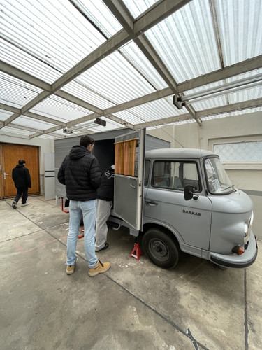 KI generiert: Das Bild zeigt Menschen, die sich ein traditionelles Barkas-Kleintransporter-Modell in einer Garage ansehen. Zwei Personen stehen an der geöffneten Seitentür des Fahrzeugs.