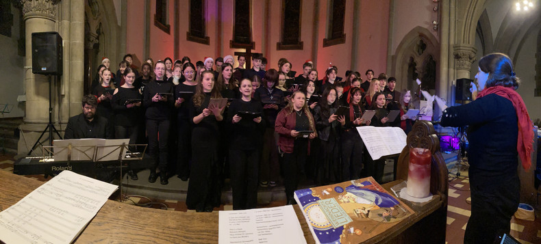 KI generiert: Das Bild zeigt einen Chor, der in einer Kirche vor Publikum auftritt. Eine Person dirigiert den Chor, während ein Pianist am Keyboard begleitet.