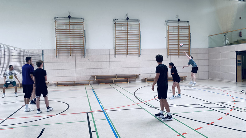 KI generiert: Das Bild zeigt eine Gruppe von Personen, die in einer Sporthalle Volleyball spielen. Eine Person ist gerade dabei, den Ball zu servieren.
