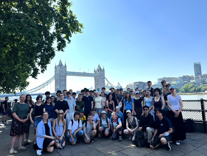 KI generiert: Eine große Gruppe von Menschen posiert für ein Foto vor der Tower Bridge in London. Im Hintergrund sind der Fluss und städtische Gebäude zu sehen.