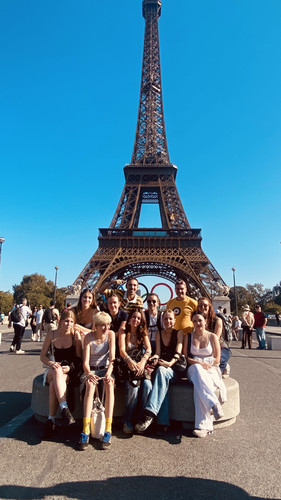KI generiert: Das Bild zeigt eine Gruppe von Menschen, die vor dem Eiffelturm in Paris posiert. Im Hintergrund sind die olympischen Ringe sichtbar.