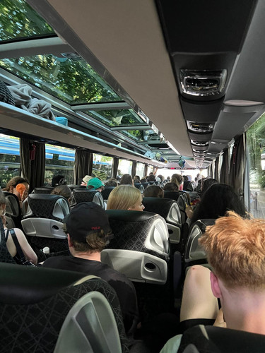KI generiert: Das Bild zeigt das Innere eines Reisebusses, in dem viele Menschen auf ihren Sitzen verteilt sind und nach vorne blicken. Durch die Fenster ist draußen die Umgebung erkennbar, wodurch ein sonniger Tag suggeriert wird.